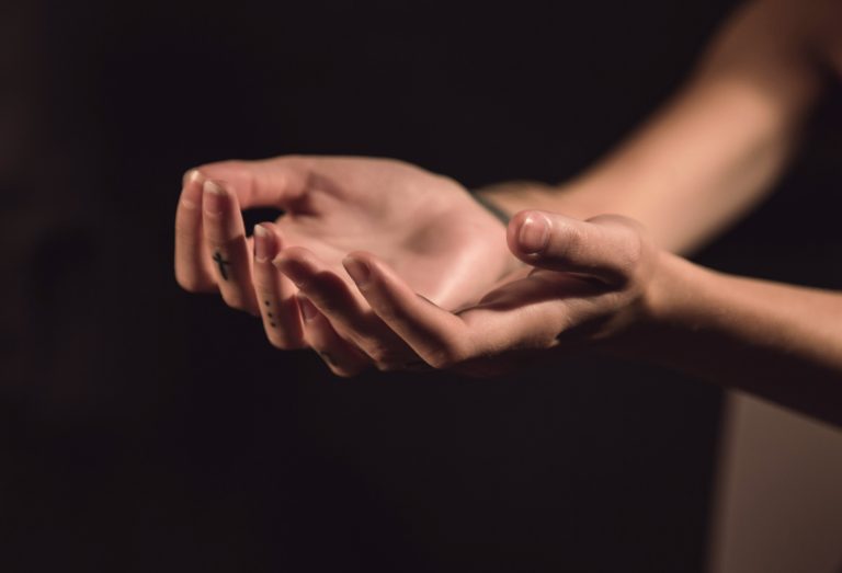 Close-up of cupped hands in a dark setting, palms upward as if offering or holding something delicate.